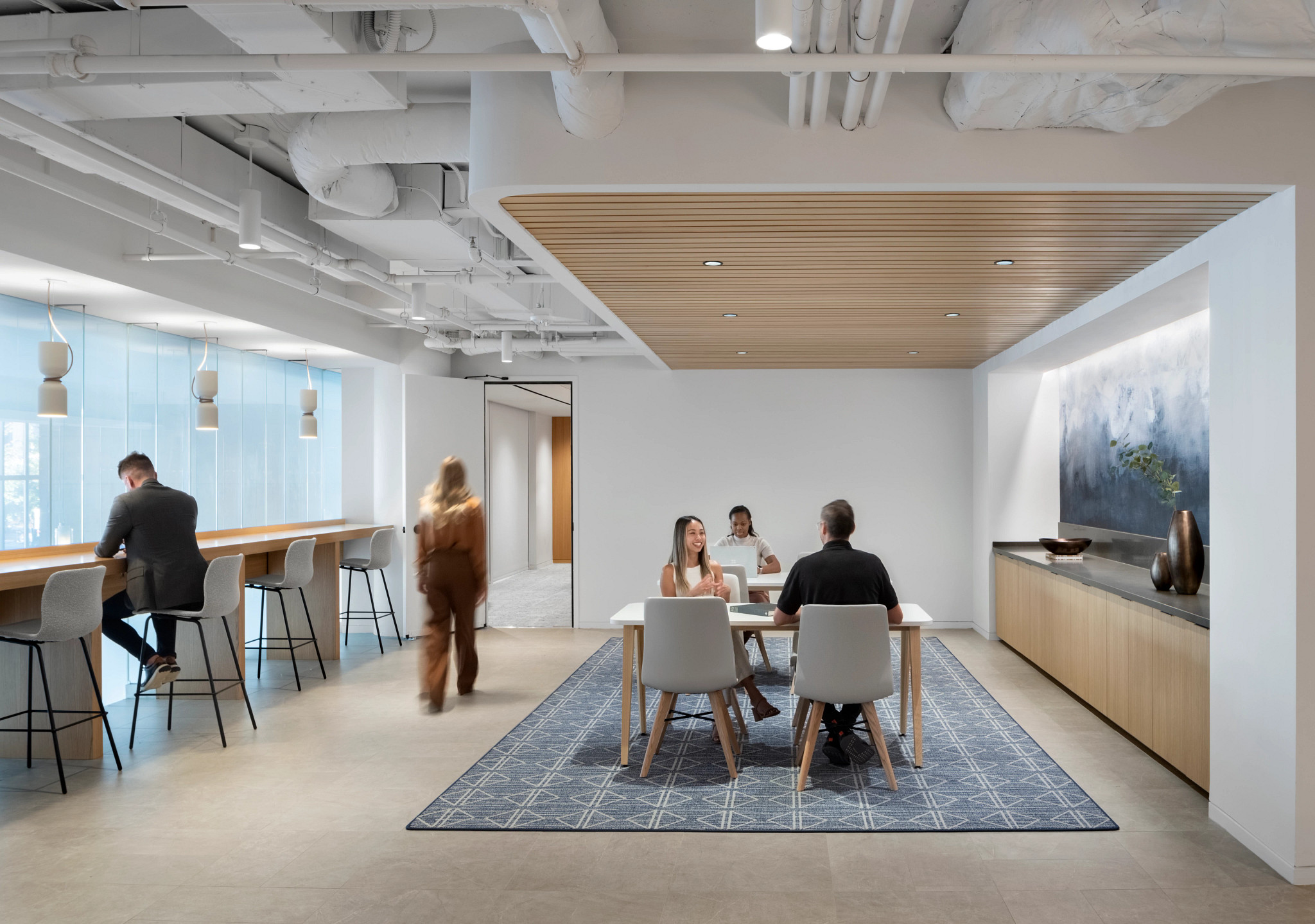 Modern workplace lounge area with a 12x15 ft area rug featuring a geometric pattern, surrounded by people working and conversing.