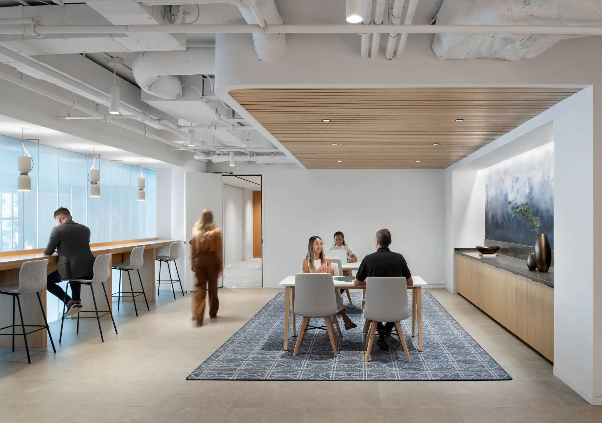 Modern workplace lounge area with a 12x15 ft area rug featuring a geometric pattern, surrounded by people working and conversing.