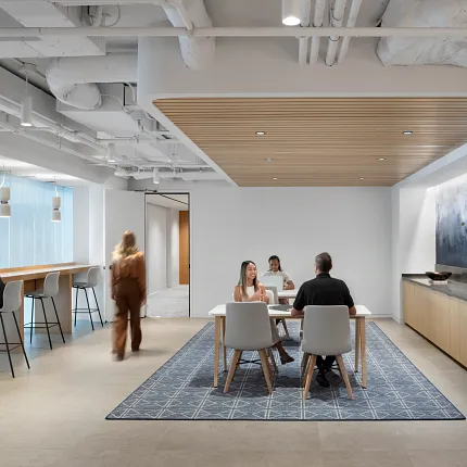 Modern workplace lounge area with a 12x15 ft area rug featuring a geometric pattern, surrounded by people working and conversing.