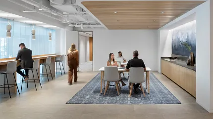 Workplace Lounge with Geometric Pattern Area Rug - 12x15 ft Modern workplace lounge area with a 12x15 ft area rug featuring a geometric pattern, surrounded by people working and conversing.