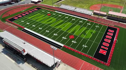 Artificial Turf Sports Field with Stadium Seating and Running Track Aerial view of a sports field with artificial turf featuring green and white markings