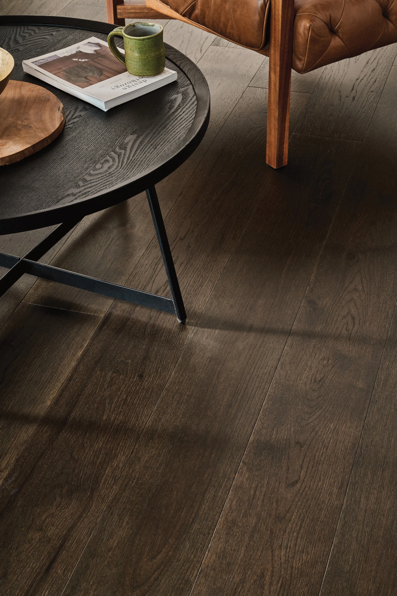 Dark brown hardwood flooring in a living room with a black round table and a leather sofa