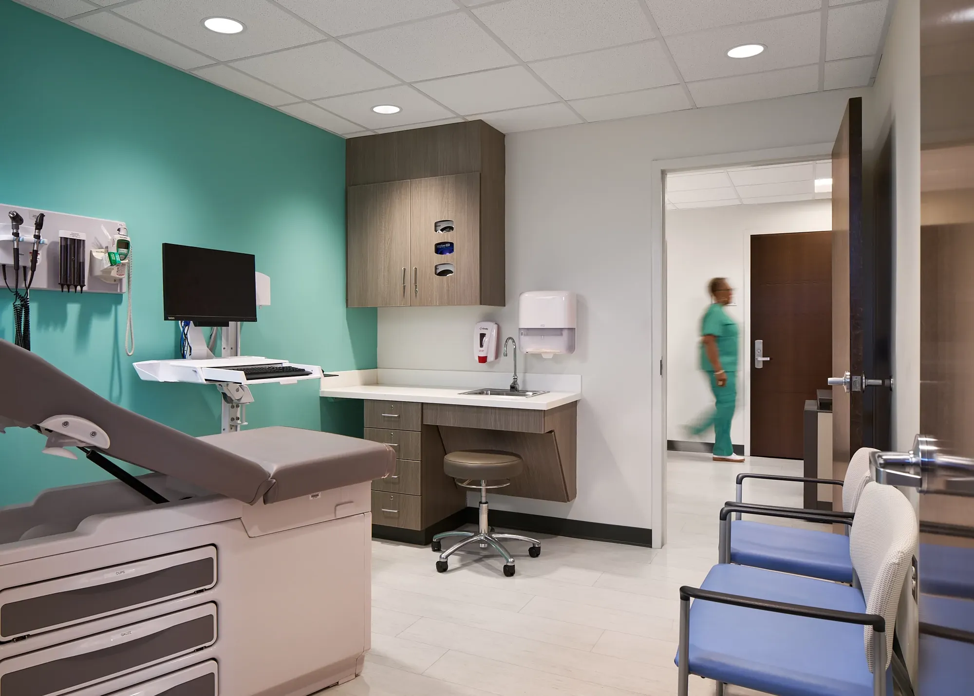 Modern healthcare facility examination room with teal accent wall, medical equipment, and light-colored flooring
