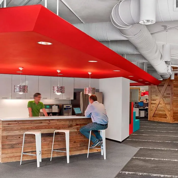 Modern workplace kitchen area with red ceiling, wooden bar counter, and commercial carpet tile flooring