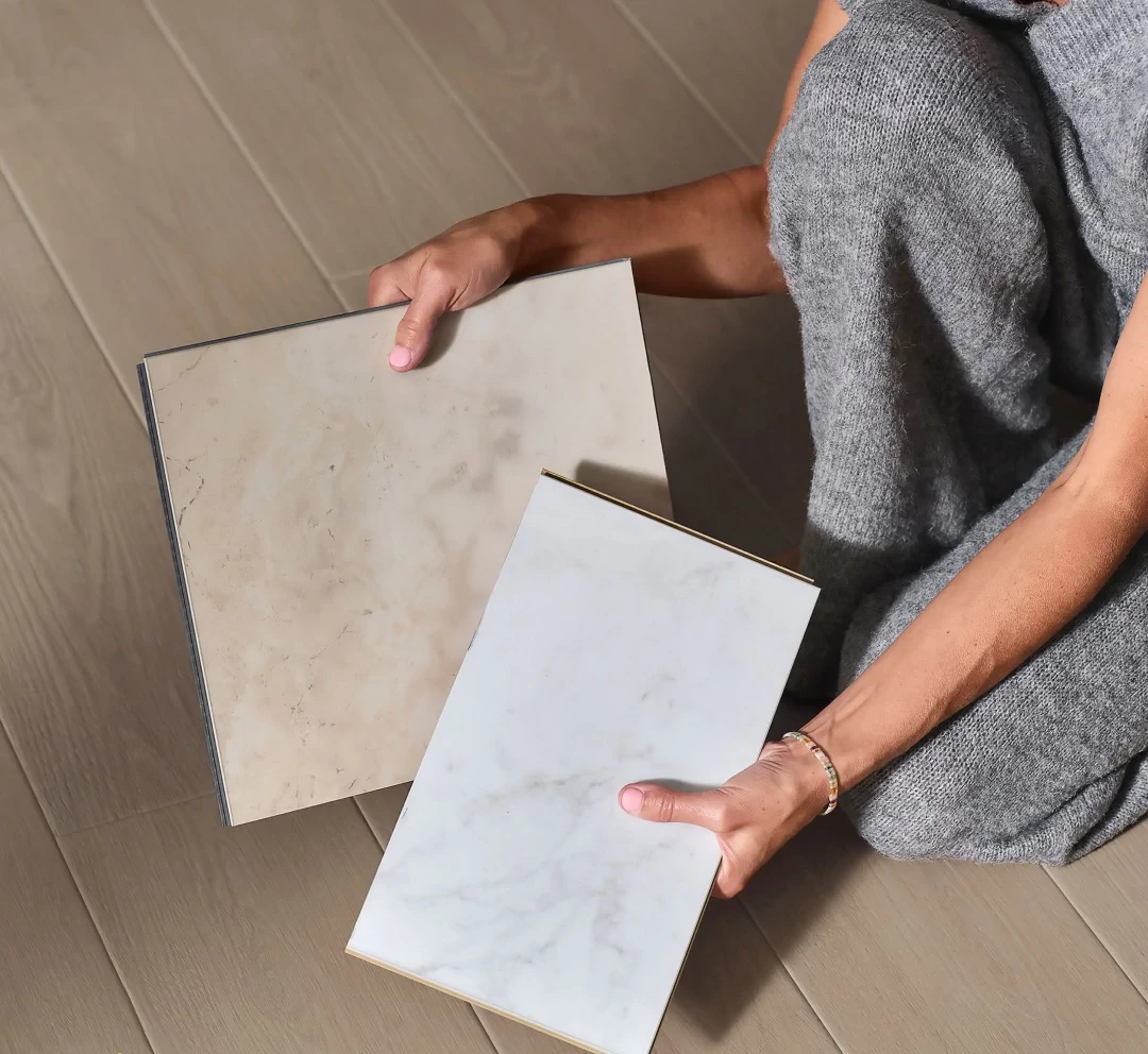 Person holding beige and white stone look luxury vinyl tile samples on wood look vinyl flooring