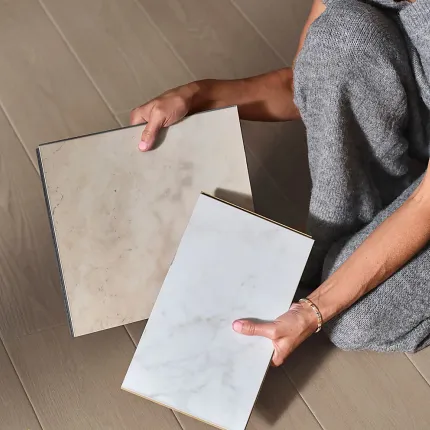 Stone Look Luxury Vinyl Tile Samples on Wood Look Vinyl Flooring Person holding beige and white stone look luxury vinyl tile samples on wood look vinyl flooring
