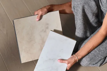 Stone Look Luxury Vinyl Tile Samples on Wood Look Vinyl Flooring Person holding beige and white stone look luxury vinyl tile samples on wood look vinyl flooring