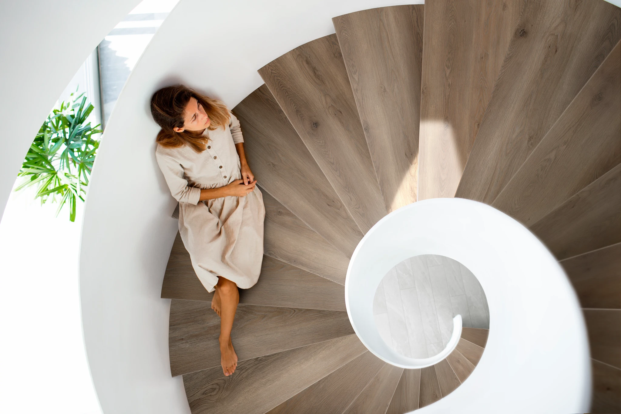 Spiral staircase with wood-look luxury vinyl plank flooring and a woman in a beige dress sitting on the steps
