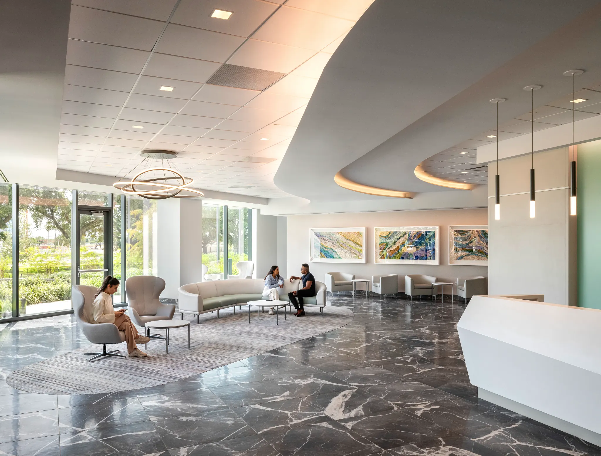 Modern healthcare facility lobby with sleek white reception desk, contemporary seating, and large windows showcasing a view of greenery, featuring elegant dark marble flooring.