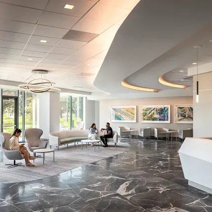 Healthcare Facility Lobby with Dark Marble Flooring and Modern Design Modern healthcare facility lobby with sleek white reception desk, contemporary seating, and large windows showcasing a view of greenery, featuring elegant dark marble flooring.