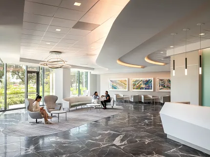 Healthcare Facility Lobby with Dark Marble Flooring and Modern Design Modern healthcare facility lobby with sleek white reception desk, contemporary seating, and large windows showcasing a view of greenery, featuring elegant dark marble flooring.