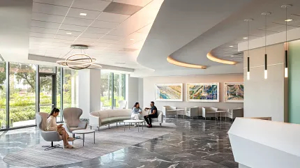 Healthcare Facility Lobby with Dark Marble Flooring and Modern Design Modern healthcare facility lobby with sleek white reception desk, contemporary seating, and large windows showcasing a view of greenery, featuring elegant dark marble flooring.