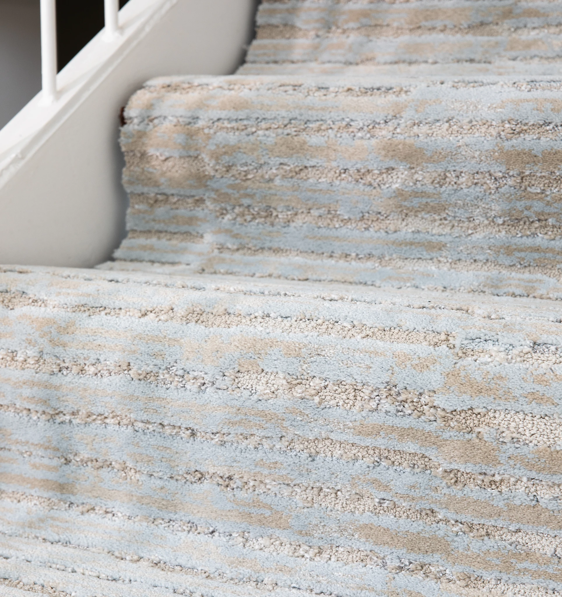 Close-up of carpeted stairs featuring a textured pattern in light blue and beige colors
