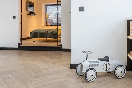 Wood Look Luxury Vinyl Plank Flooring in Herringbone Pattern for Modern Homes living space with wood look luxury vinyl plank floor in a herringbone pattern with a white toy car and a view into a bedroom