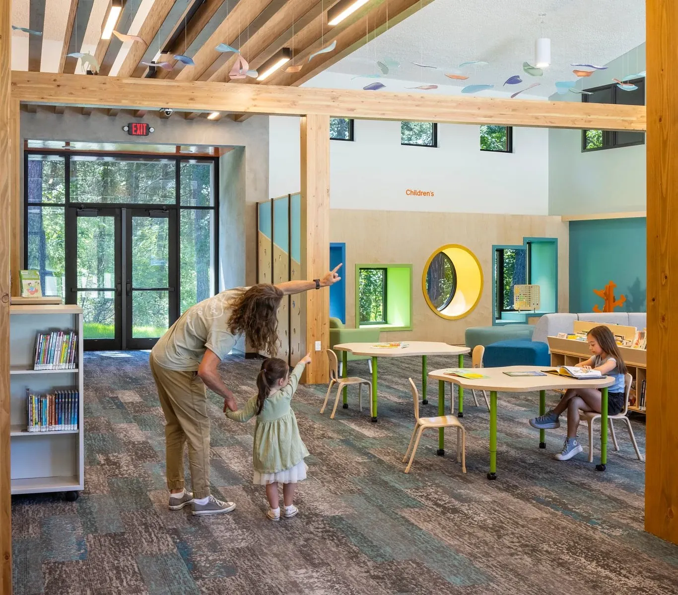 A woman looking at what a child is pointing to up in the sky, looking at the hanging fixtures in the library 