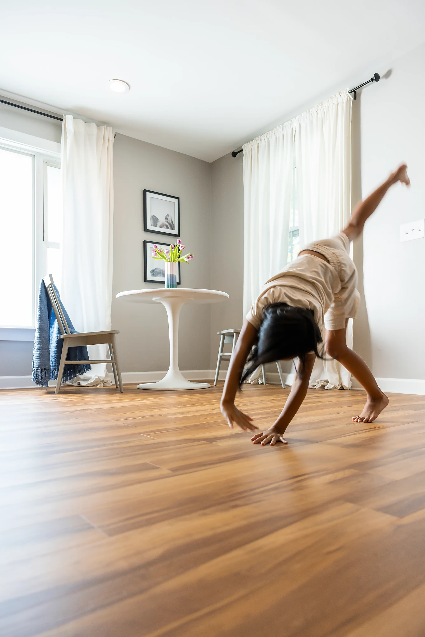 Child doing a cartwheel on wood look vinyl flooring in a bright room with white curtains and modern furniture