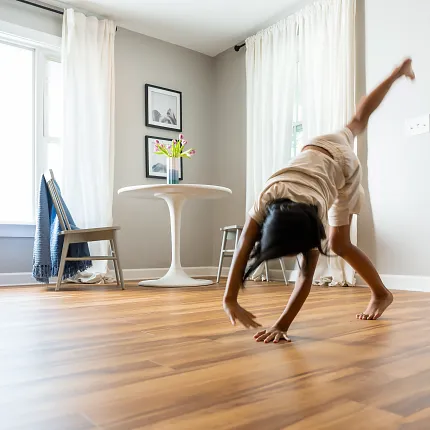 Coretec Residential WPC Wood Look Vinyl Flooring - 48.03x4.96 inch Child doing a cartwheel on wood look vinyl flooring in a bright room with white curtains and modern furniture