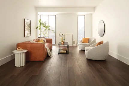 Contemporary Living Room with Wood Look Luxury Vinyl Plank Flooring. living room with dark wood look luxury vinyl plank floor with a brown leather sofa white round chairs and large windows