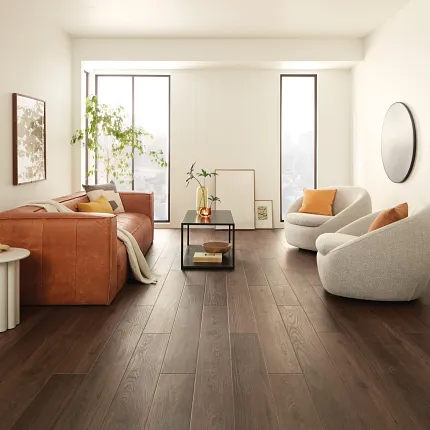 Contemporary Living Room with Wood Look Luxury Vinyl Plank Flooring. living room with dark wood look luxury vinyl plank floor with a brown leather sofa white round chairs and large windows