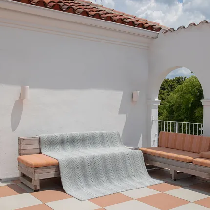 Outdoor Patio with Wooden Bench and Orange Cushions Outdoor patio with terracotta roof tiles and white walls, featuring a wooden bench with orange striped cushions and a light gray blanket