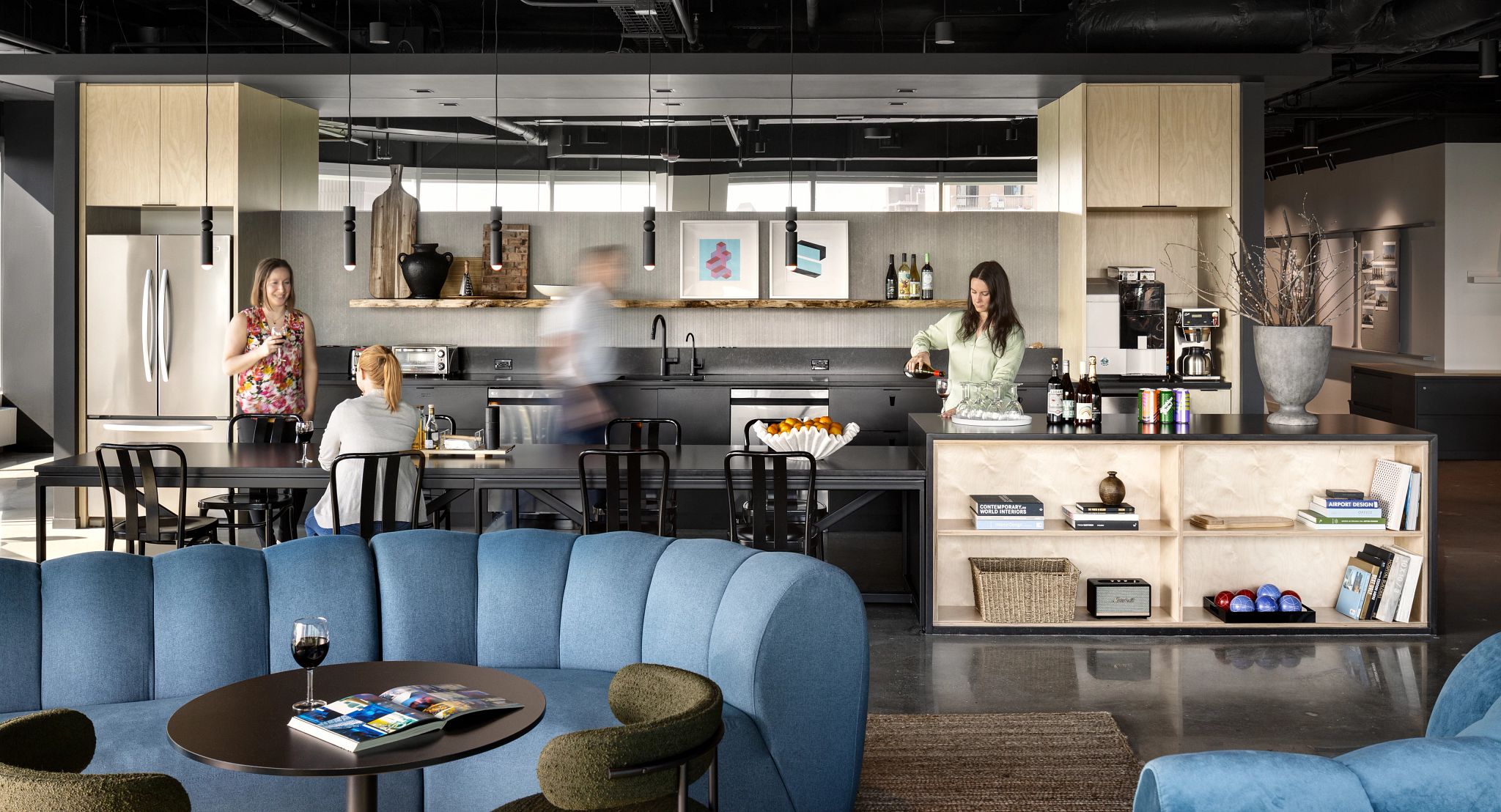 Modern workplace kitchen with sleek cabinetry, black countertops, and a blue sectional sofa