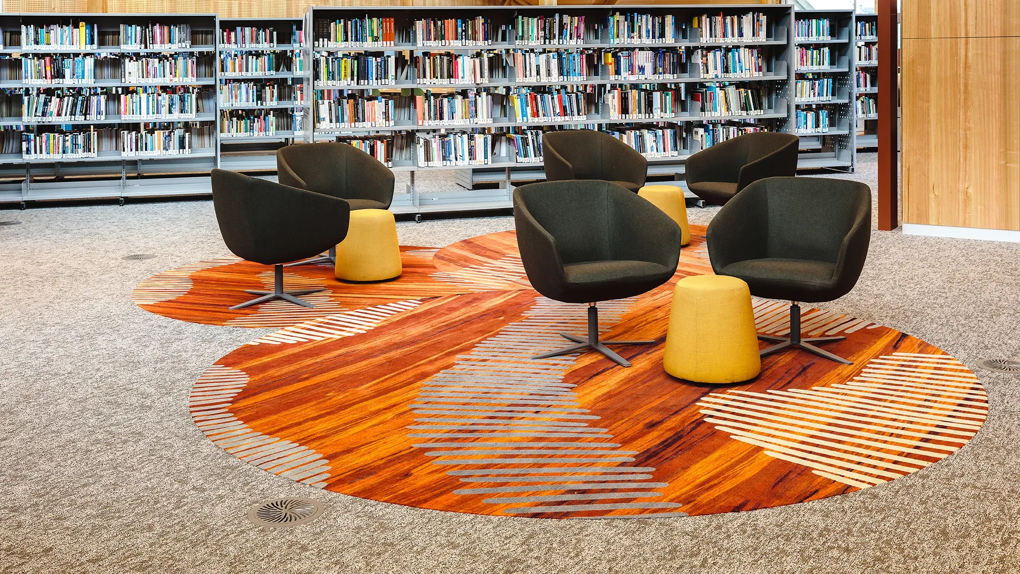 Two-person seating areas in a library with a vibrant orange rug