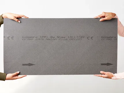 Gray flooring sample for workplace environments Two people holding a large rectangular gray flooring sample with text and arrows, suitable for workplace environments