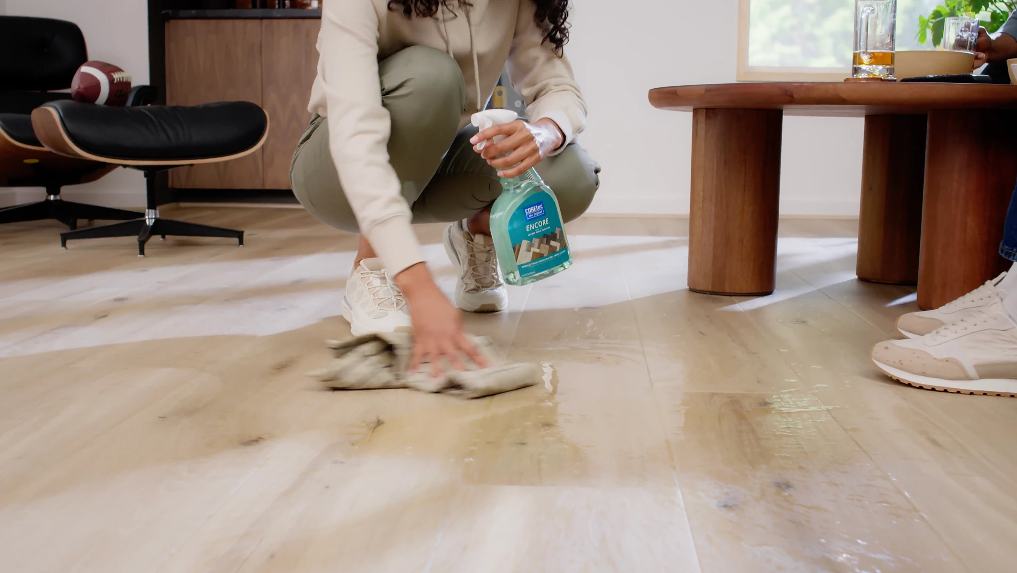 Woman cleaning light wood look vinyl flooring in a modern living room with a spray bottle and cloth