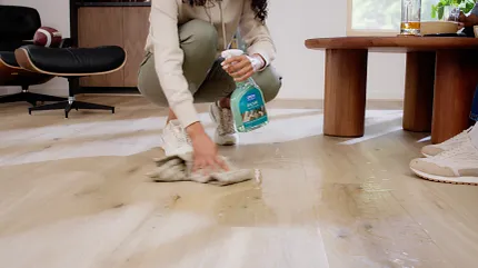 Easy to clean wood look luxury vinyl flooring in a contemporary living space Woman cleaning light wood look vinyl flooring in a modern living room with a spray bottle and cloth