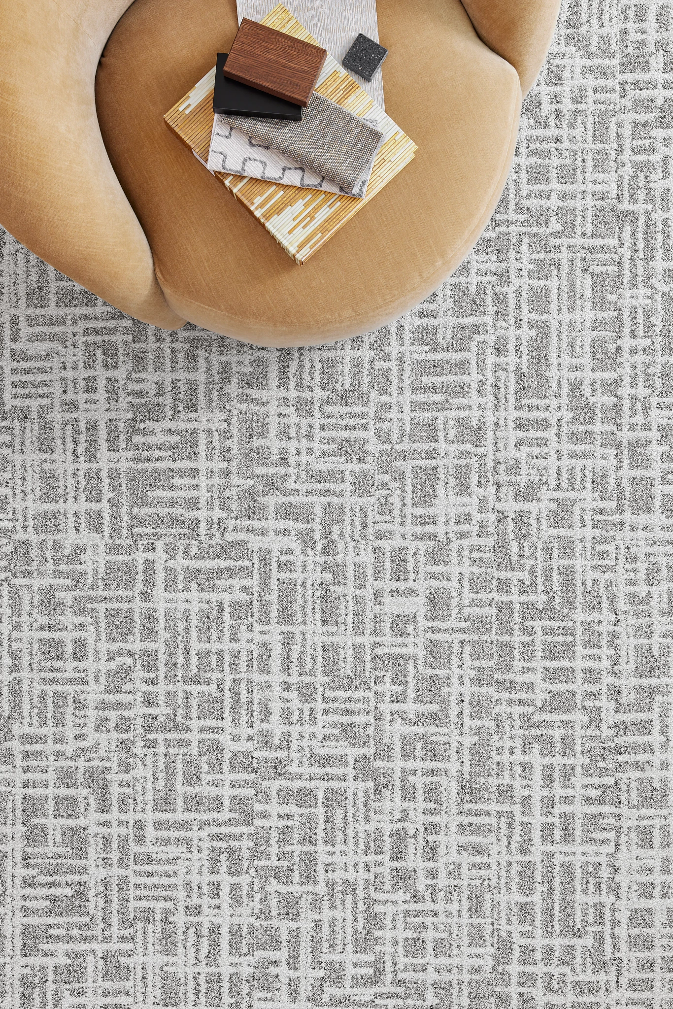 Modern geometric pattern commercial carpet tile in gray and white with a tan chair and fabric swatches