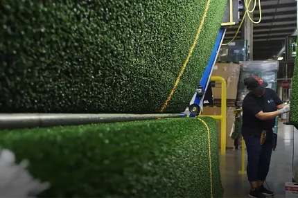 Worker inspecting large rolls of synthetic turf inside a manufacturing facility. Worker inspecting large rolls of synthetic turf inside a manufacturing facility.