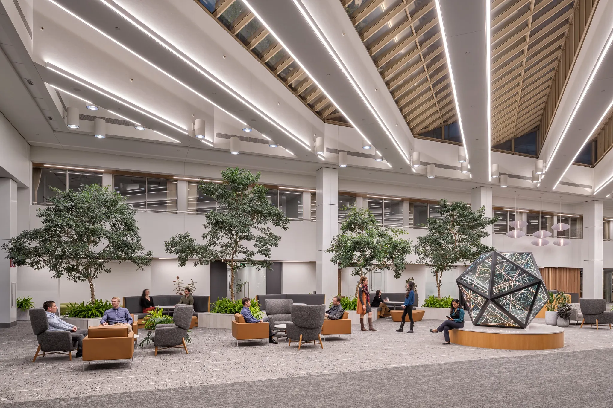 Modern workplace lobby with commercial carpet flooring, featuring contemporary seating and indoor plants under a skylit ceiling