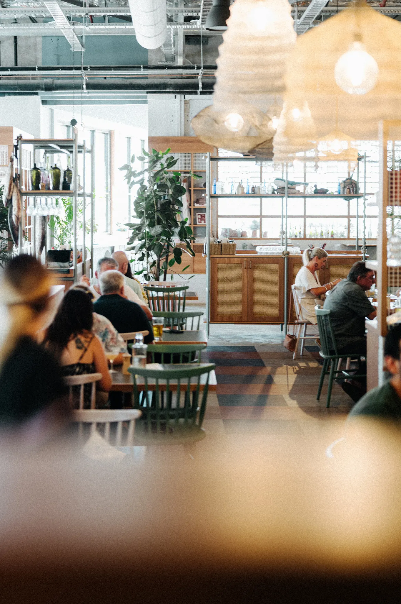 Modern restaurant interior with diverse group of people dining, featuring stylish wooden furniture and contemporary lighting