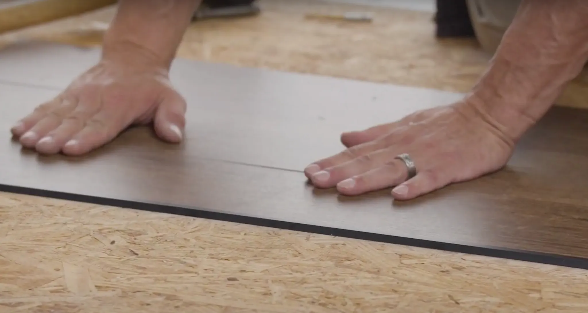 Hands installing commercial LVT flooring on plywood subfloor