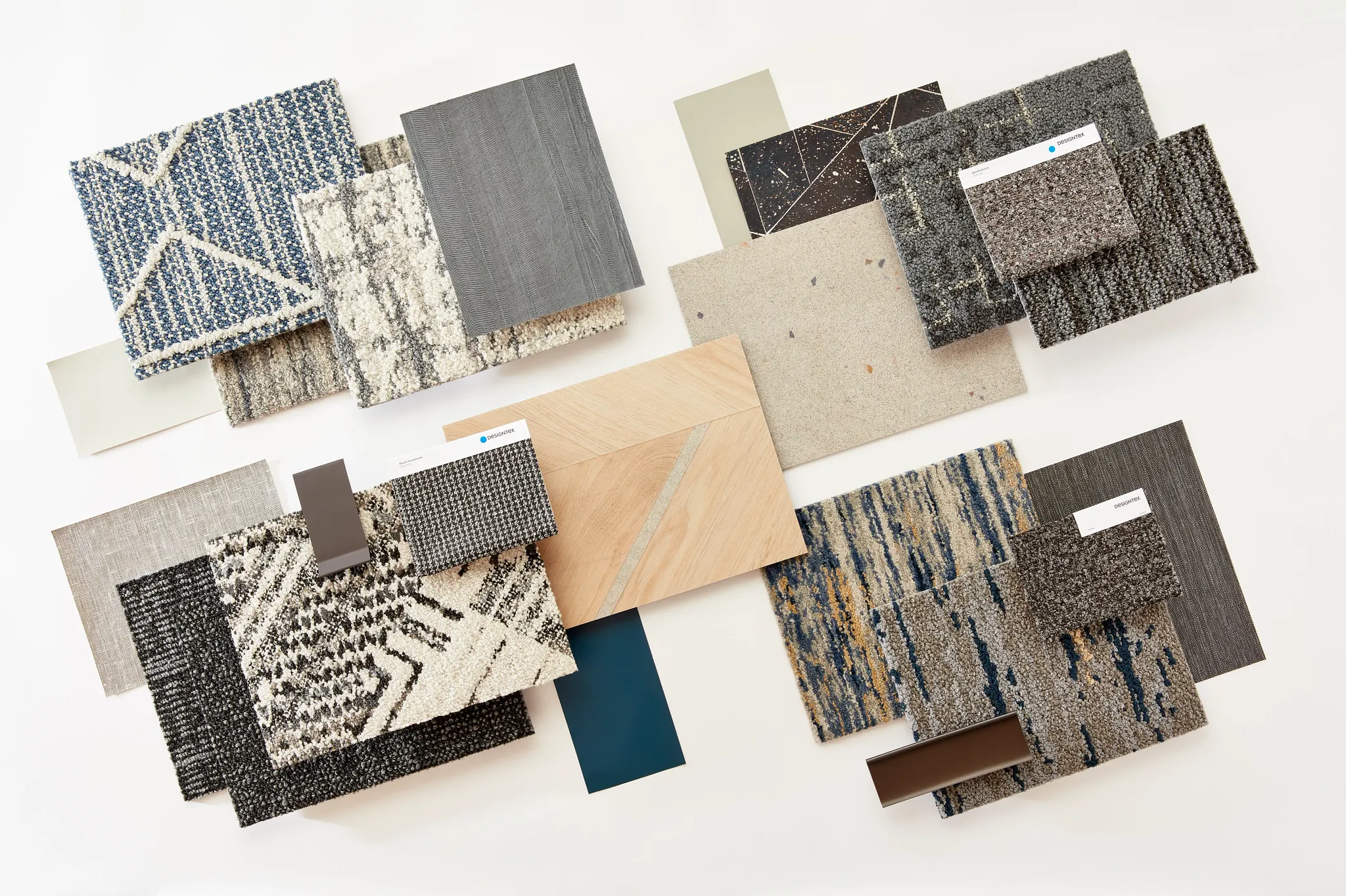 Assorted flooring swatches including commercial carpet tiles and broadloom in various patterns and colors such as blue, beige, and gray, suitable for workplace environments