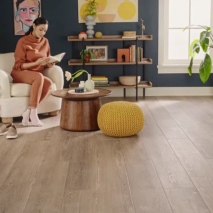 Modern Living Room with Wood Look Luxury Vinyl Plank Flooring. living room with wood look luxury vinyl plank floor with a woman reading on a white armchair surrounded by decor and plants