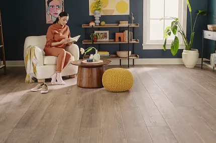 Modern Living Room with Wood Look Luxury Vinyl Plank Flooring. Cozy living room with wood look luxury vinyl plank flooring, featuring a woman reading on a white armchair, surrounded by modern decor and plants.