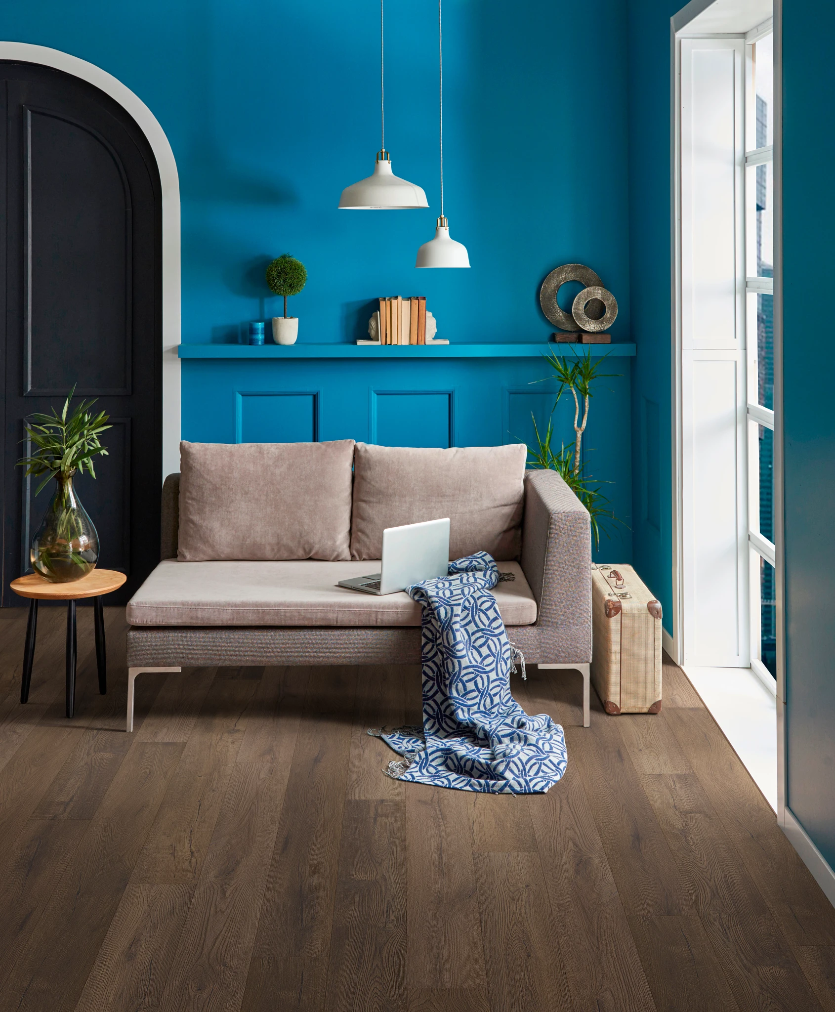 living room with arched doorway, vivid blue walls a tan settee with a throw. Dark brown wood look vinyl on the floor