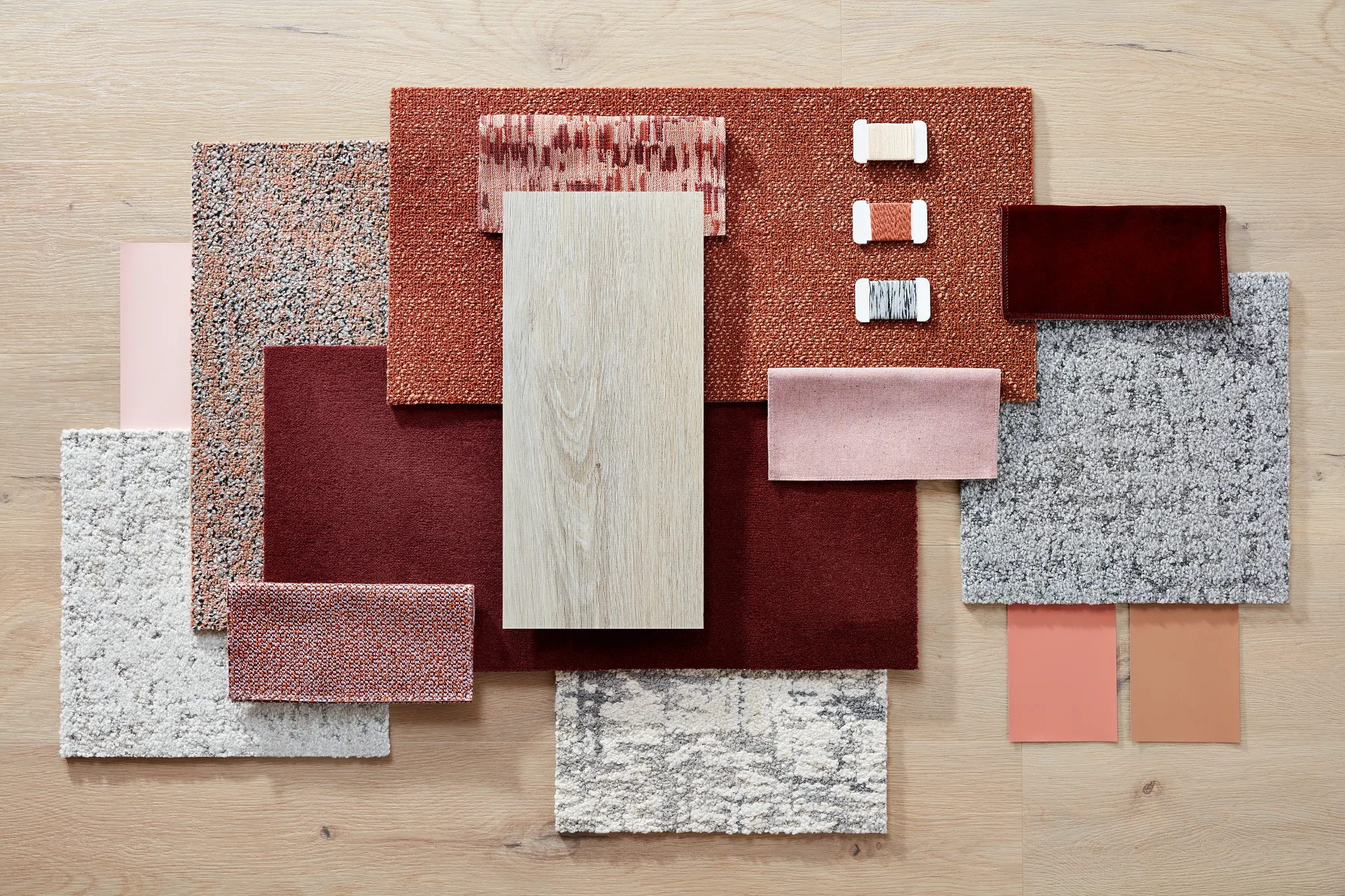 Assorted flooring swatches including red, pink, gray, and beige tones on a light wood background