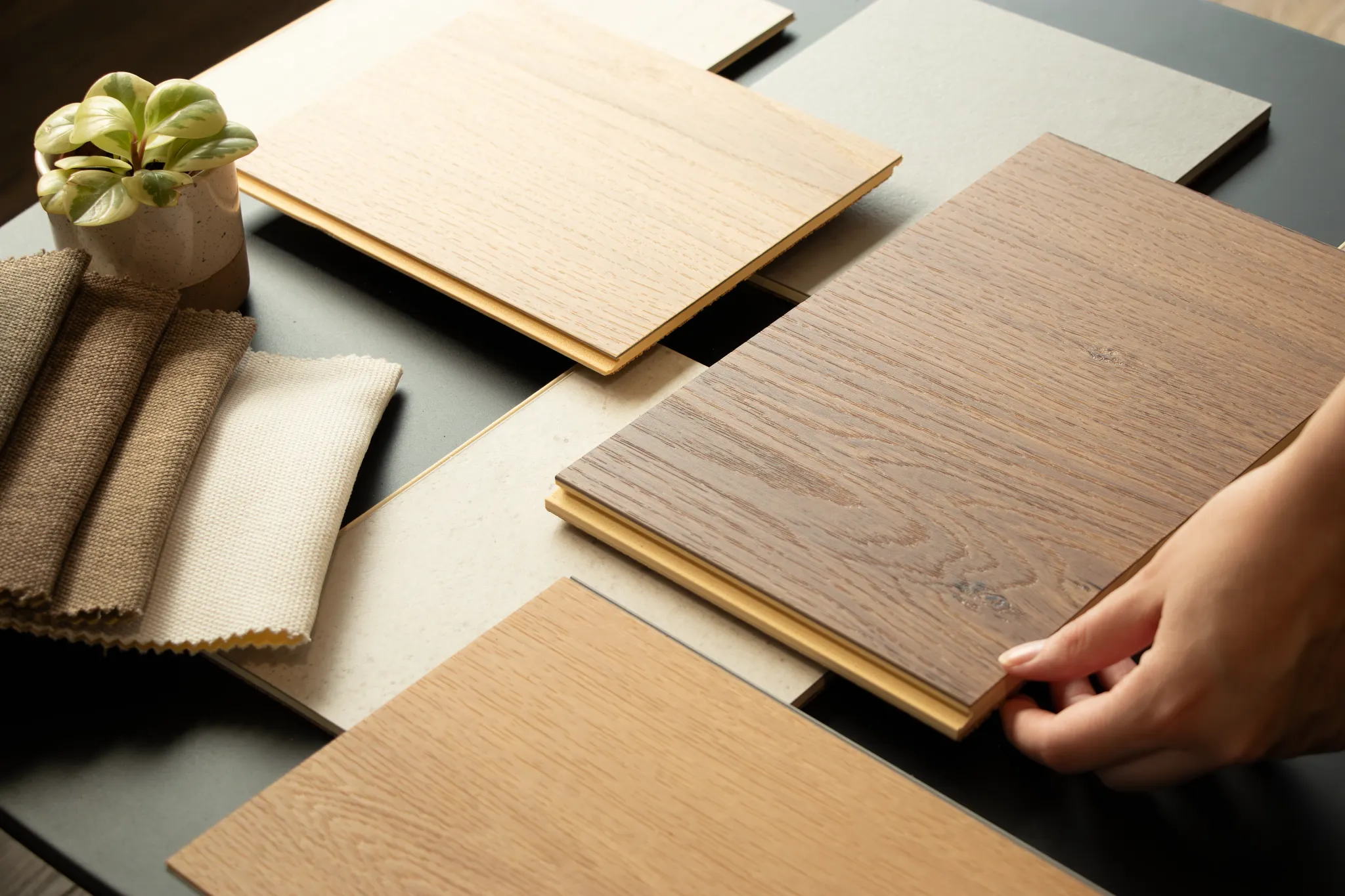 Coretec wood and tile floor samples on table with hand and plant