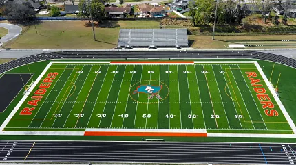 High school football field with track and bleachers Aerial view of a football field with "Raiders" branding