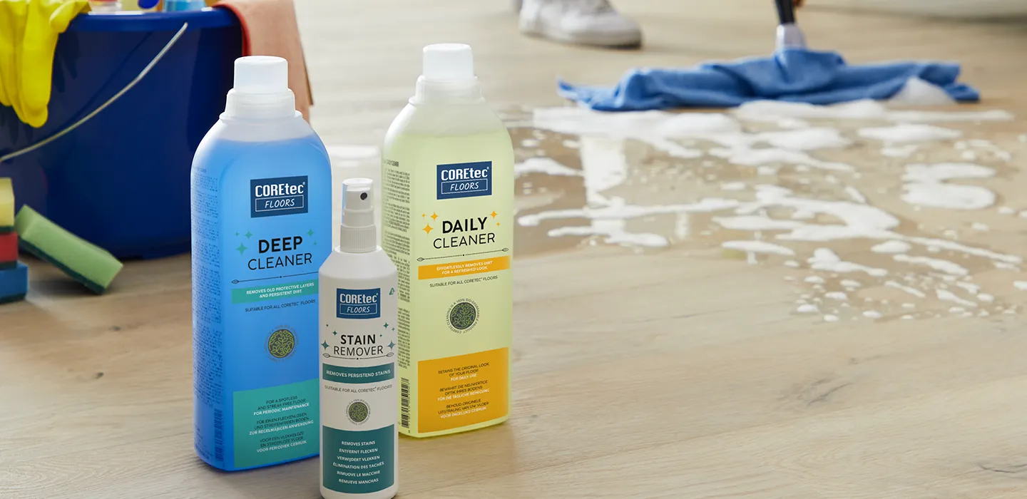 Cleaning products on light wood look vinyl flooring with a mop and bucket in the background