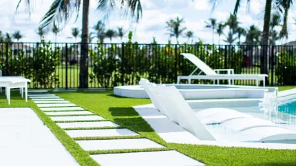 Stylish poolside design with lush greenery and seating Modern outdoor pool area with white lounge chairs and green grass
