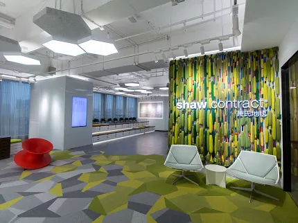 Shaw Contract Office Space with Geometric Patterned Carpet in Green, Gray, and Yellow Modern office space with geometric patterned carpet in shades of green, gray, and yellow, featuring Shaw Contract branding on a vibrant wall