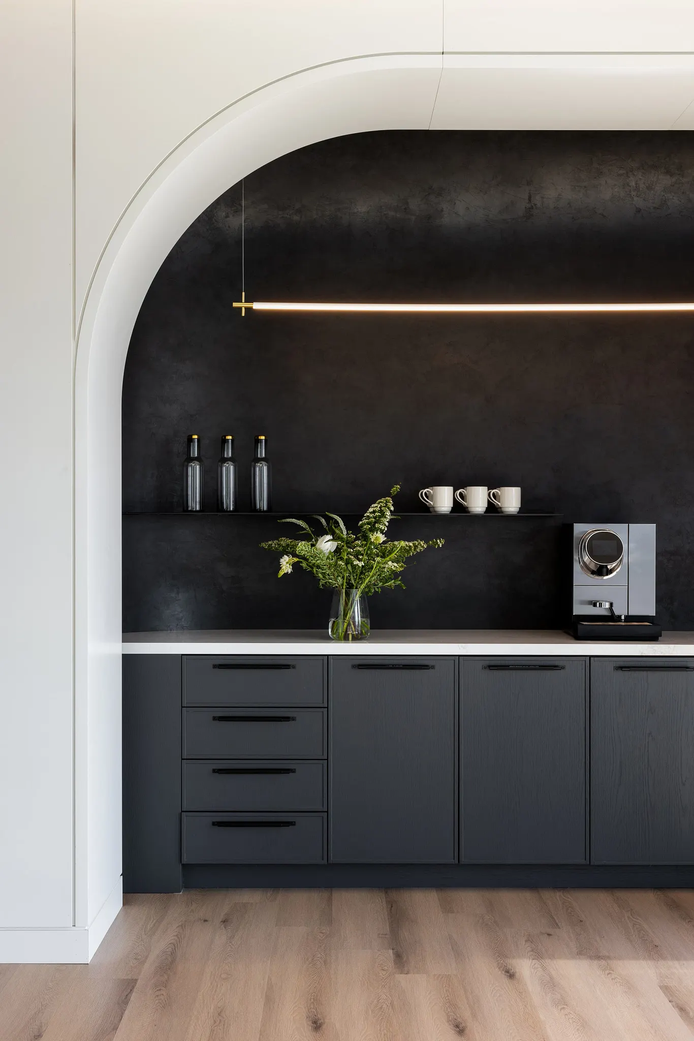 Modern kitchen with light wood flooring, dark cabinetry, and minimalist decor in a workplace setting