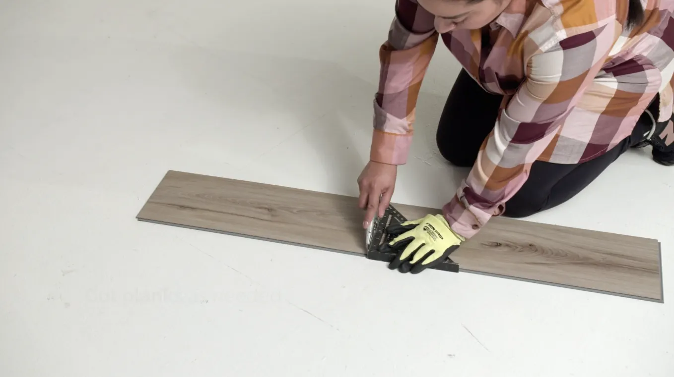 Person installing wood-look flooring plank on white surface
