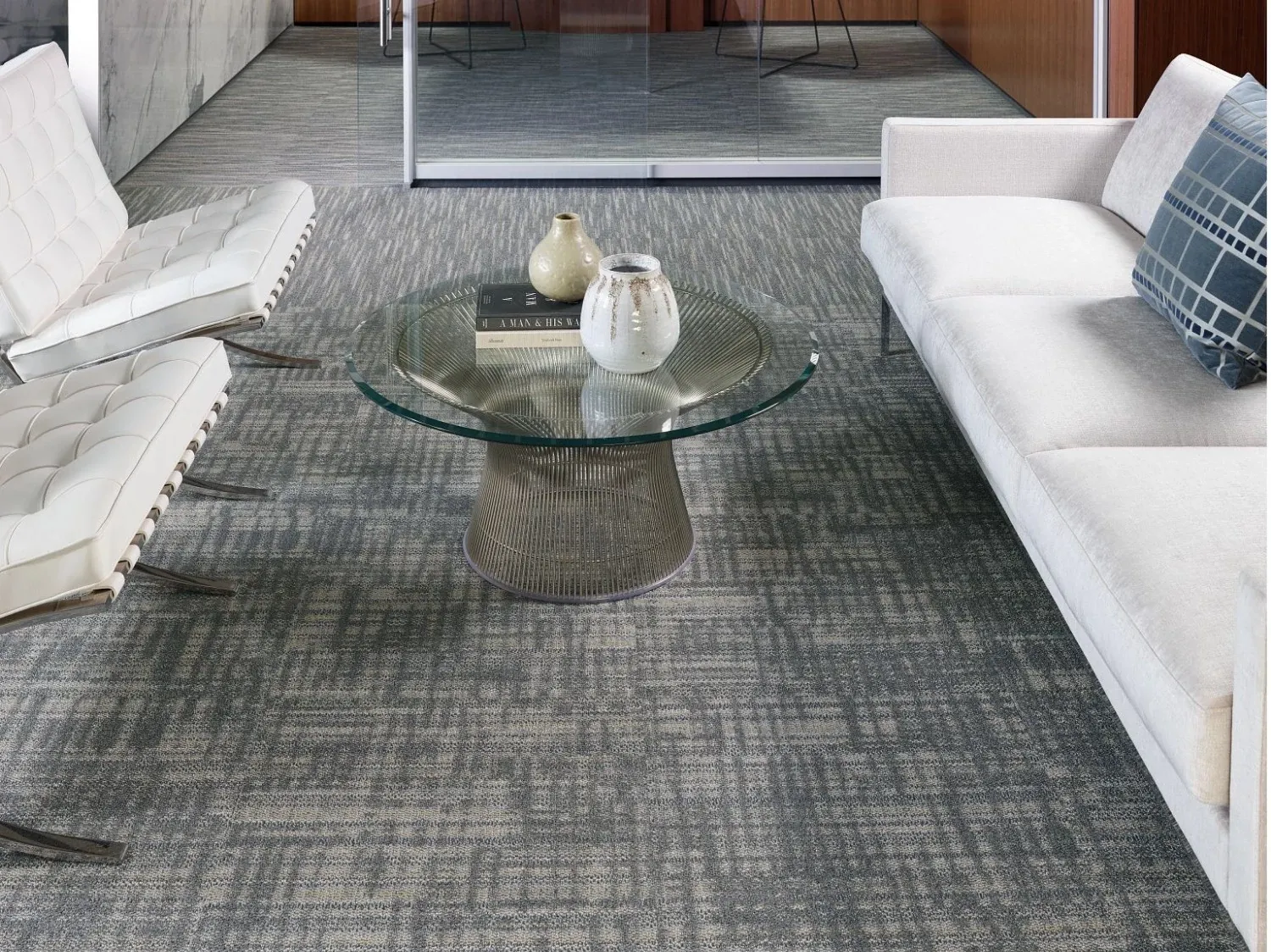 Modern office lounge with glass coffee table and white seating on gray patterned commercial carpet tile
