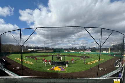 Artificial Turf Baseball Field with Players Practicing Baseball field with artificial turf and players practicing under a cloudy sky