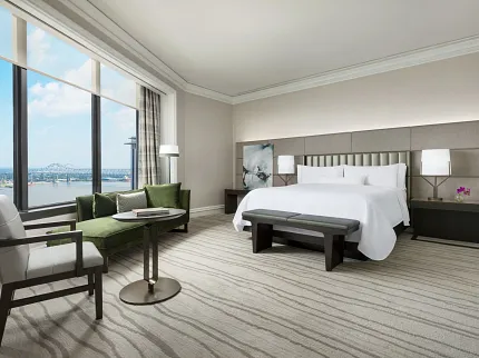 Elegant Hospitality Room with Striped Carpet Flooring and River View. Modern hotel room with a large bed, green sofa, and a view of the river, featuring elegant striped carpet flooring, Hospitality.