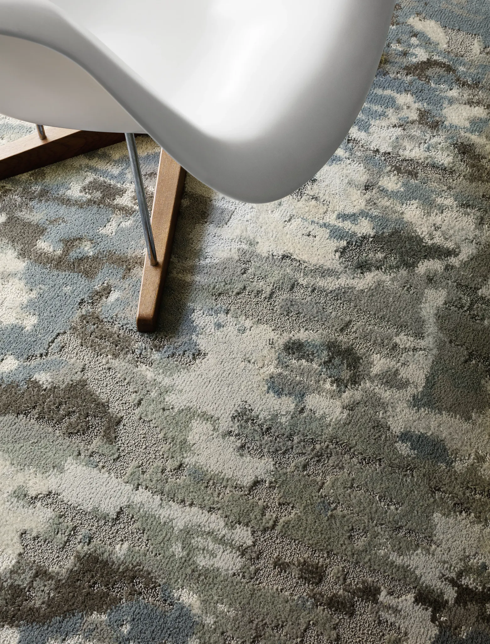 Modern white chair on abstract patterned commercial carpet tile in shades of blue, gray, and beige